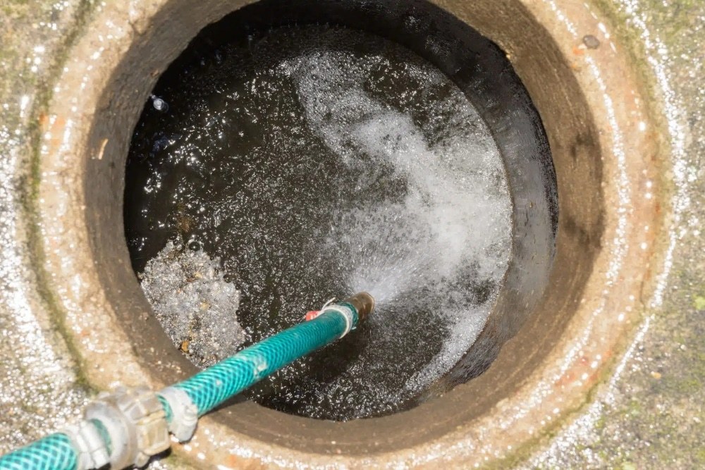 A high pressure jetting hose working inside an open sewer pit with water foaming around the nozzle