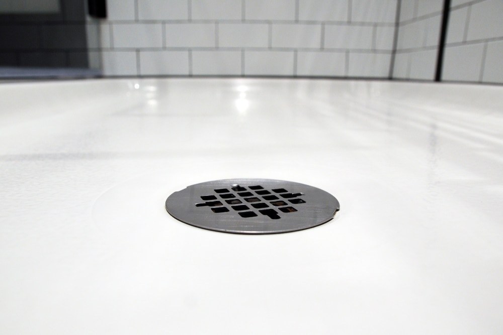 A round chrome floor waste grate set into a white tiled shower base