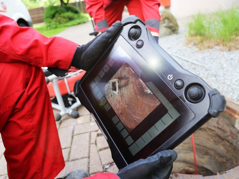 Plumber using camera to check sewer line on digital screen for hidden pipe damage.