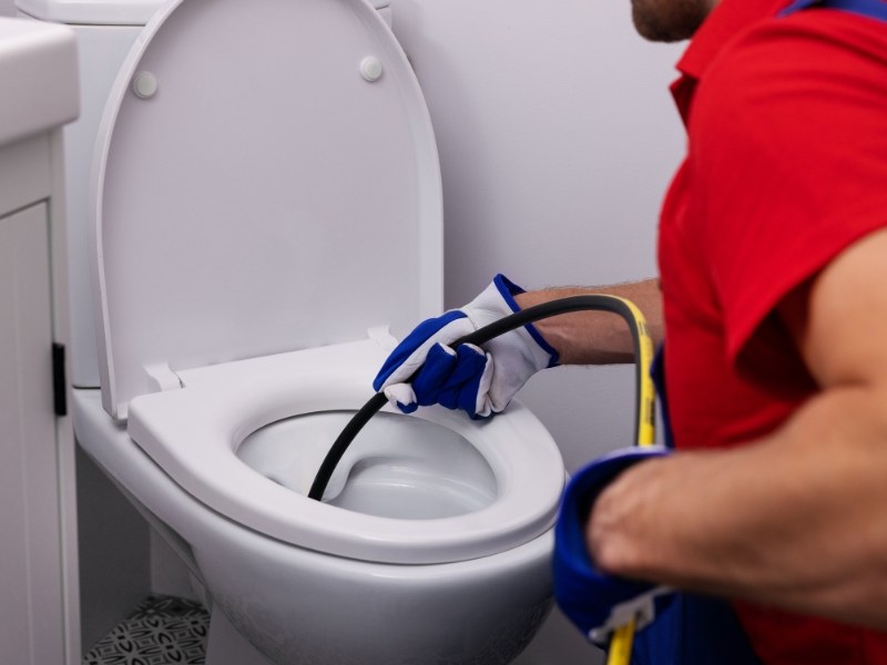 Plumber fixing a blocked toilet using a drain snake tool