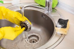 Routine drain maintenance with gloved hand cleaning kitchen sink to prevent clogs and ensure smooth water flow.
