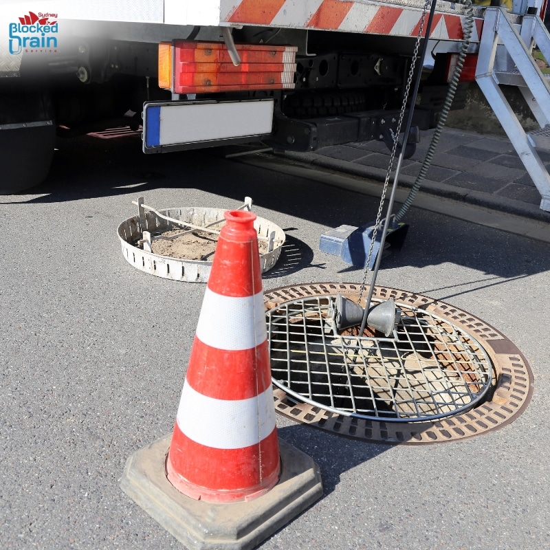 CCTV drain inspections with safety cone and camera equipment inspecting underground pipes through a manhole for blockages and damage.