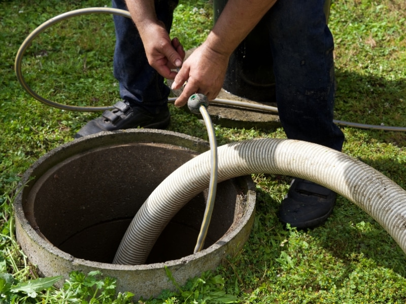 Worker fixing sewer line through inspection opening with hose and equipment